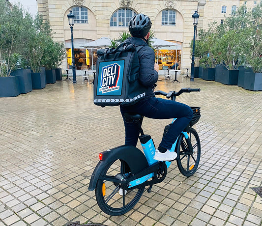 Livreur Delicity à vélo avec le sac PAKERS 74 L et le patch Delicity posé sur la face avant
